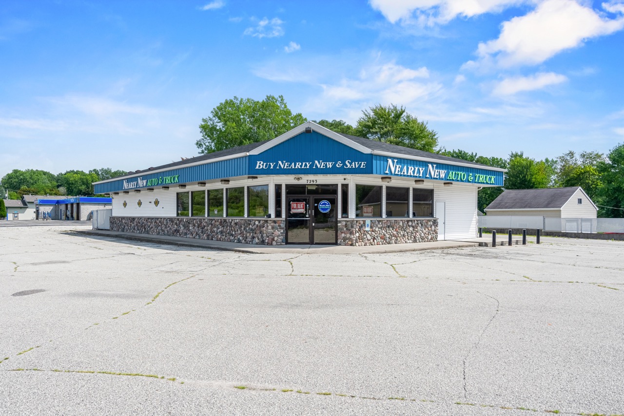 Front view of a commercial property at the corner of US Highway 10 & 114 in Menasha, featuring a stone facade, large windows, and prominent signage for Nearly New Auto & Truck.